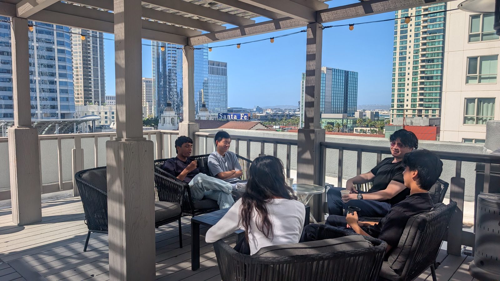 Five members of the Flashlight 3D team sit together on a rooftop patio in downtown San Diego, talking over coffee with the city skyline behind them.